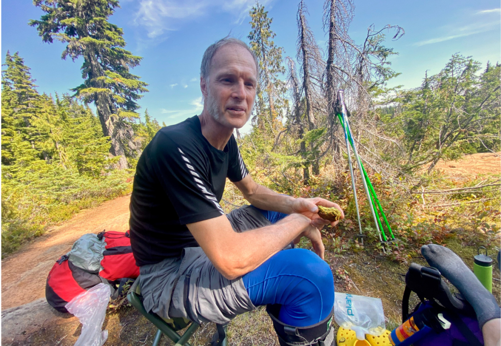 Arne Pedersen smiling with a hint of laughter on a trail break in Strathcona Park, sharing a joyful moment in nature that reflects connection and healing through shared presence.