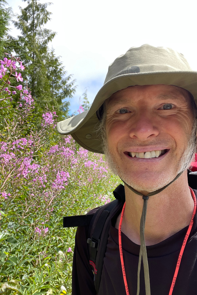 Arne Pedersen offering a warm, welcoming approach to anxiety therapy near Victoria BC, surrounded by wildflowers on a peaceful forest trail.