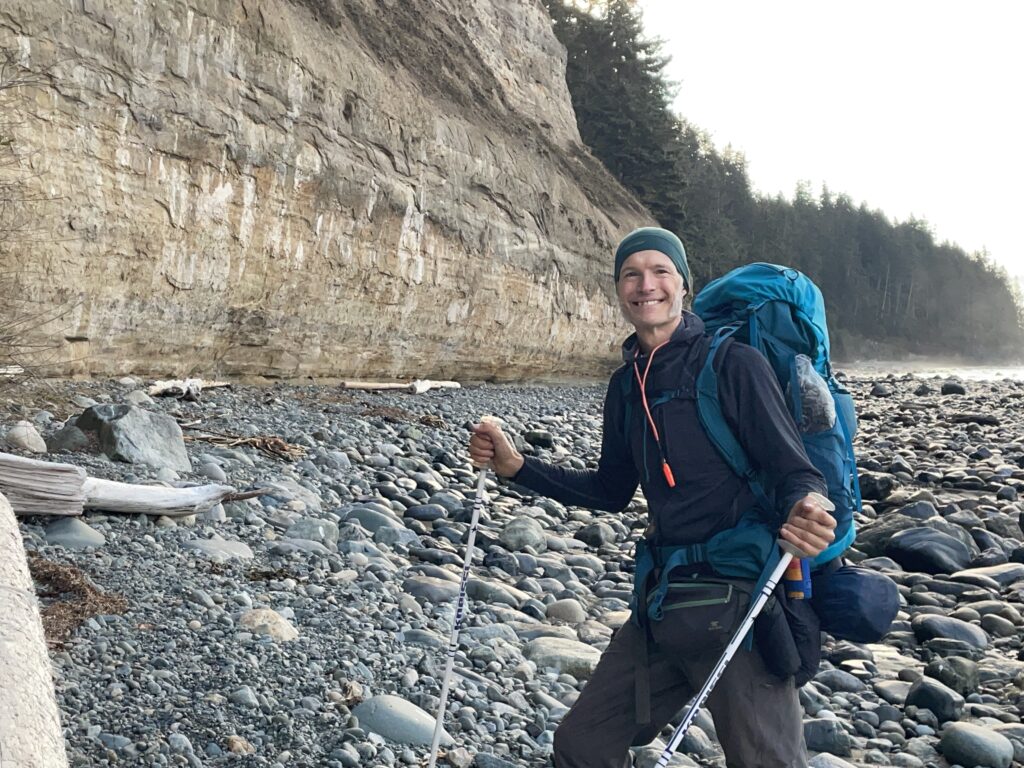 Arne Pedersen smiling while backpacking along a rocky coastline, representing confidence, resilience, and supportive steps forward in PTSD recovery.